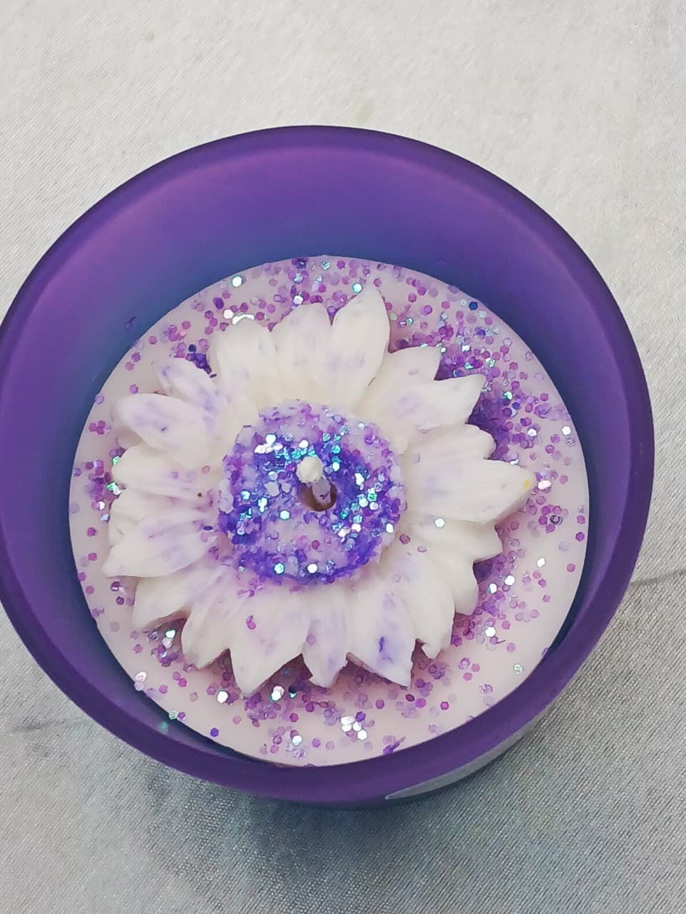 Decorative item with white flower design and purple glitter on a gray background